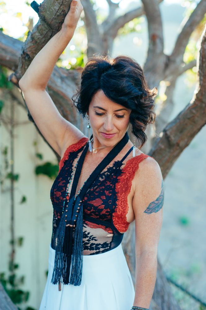 Woman smiling looking down with one arm resting on the branch above