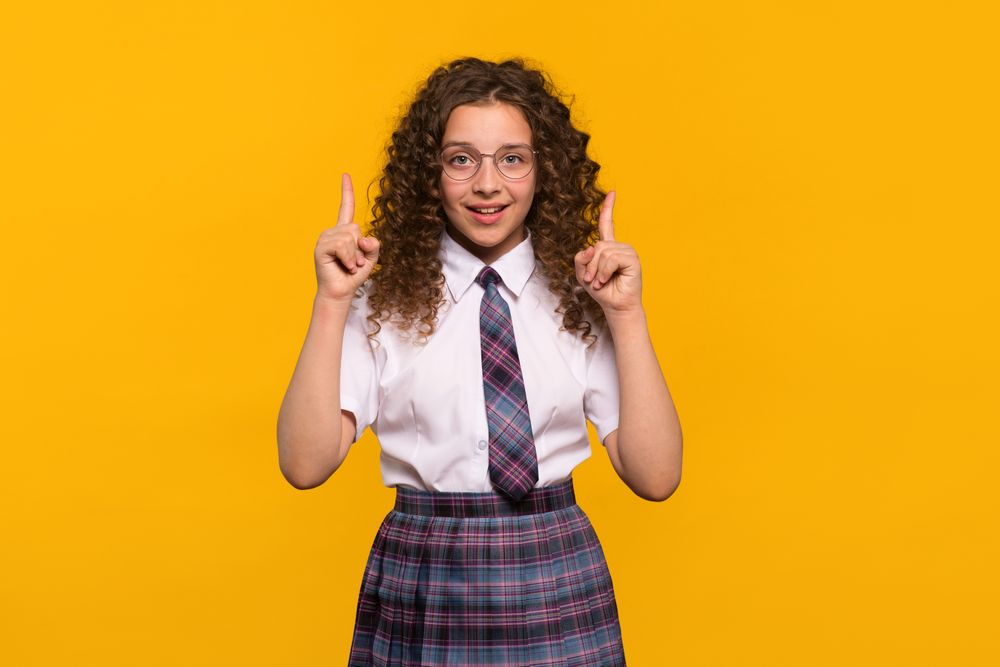 Girl wearing glasses pointing upwards with both hands