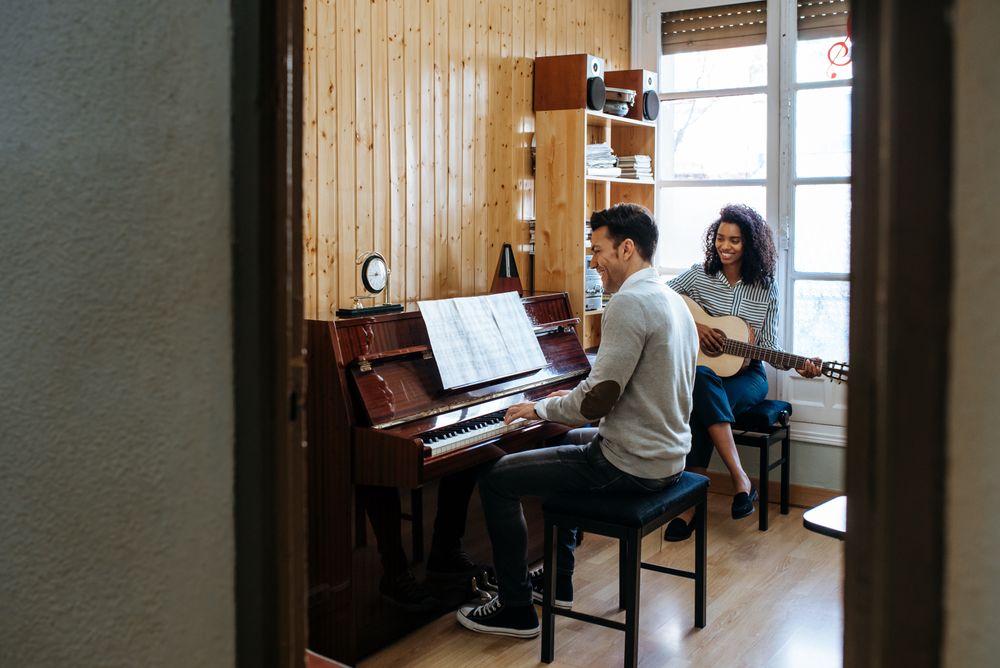 Man playing piano near woman playing guitar in studio