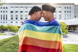 Gay couple under LGBT rainbow flag while laughing and looking at each other. Concept of Pride. Pride month.