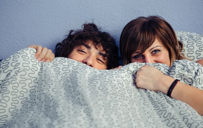 Happy couple laughing and hiding under duvet