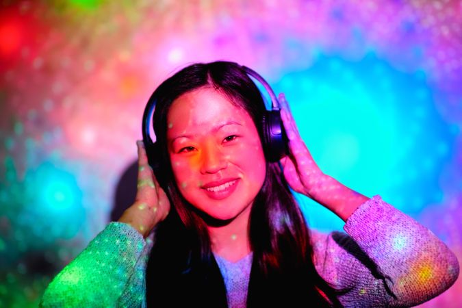 Happy Asian woman in headphones under bright illumination in stu