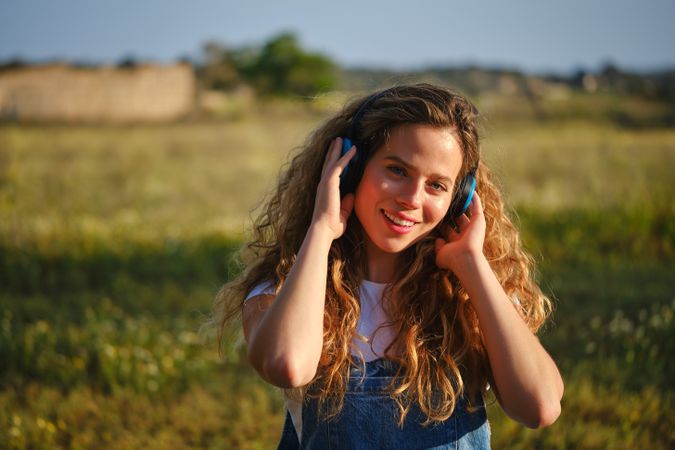Cheerful woman listening to music in headphones in countryside