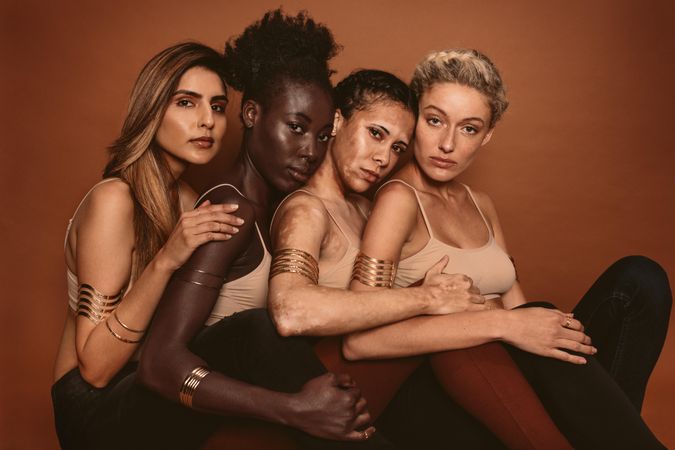 Group of diverse women sitting together against brown background