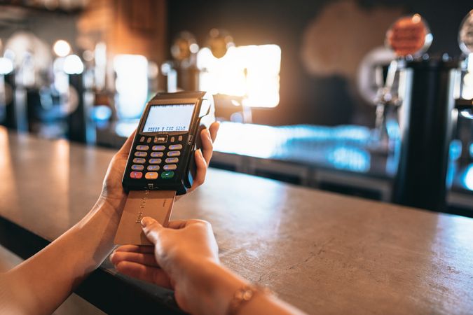 Close up of female’s hands using debit card to pay bar tab
