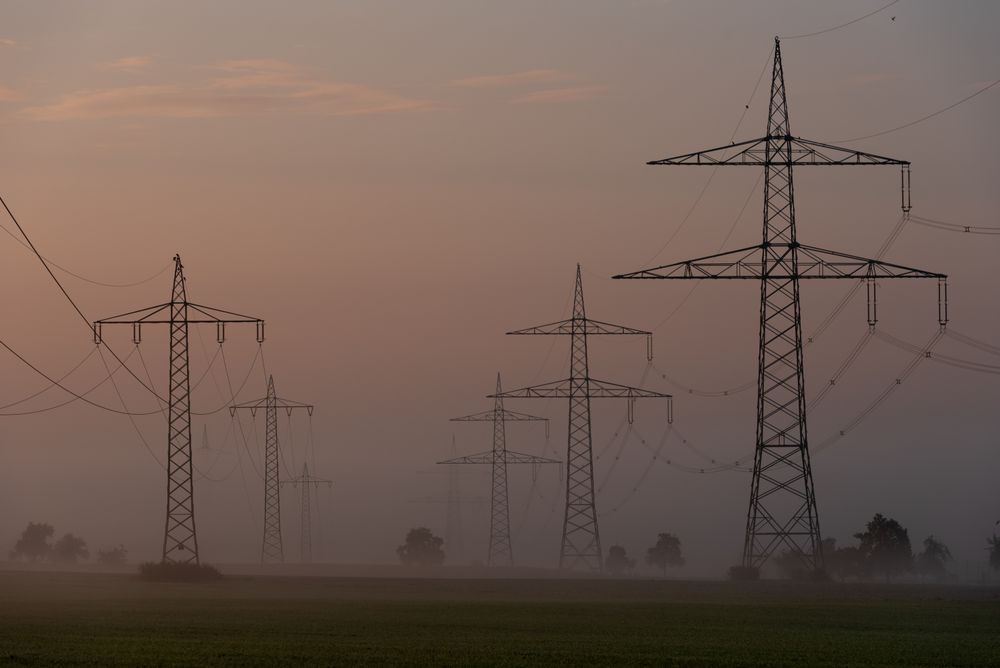 Electricity pylons on agricultural fields at golden on a foggy morning