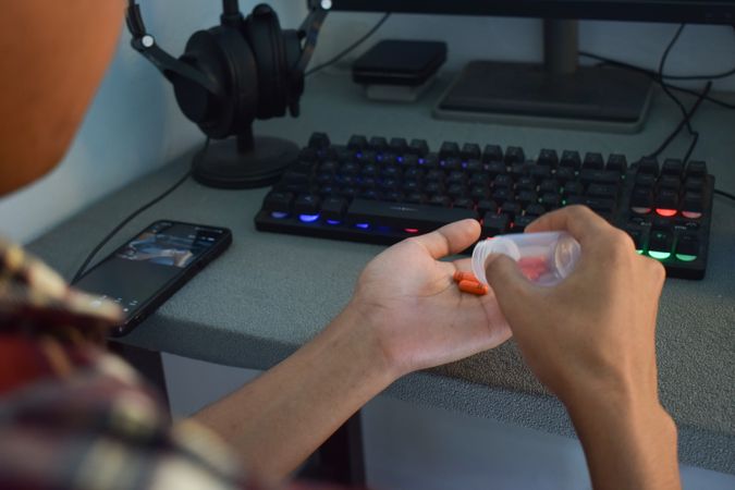 Person pouring prescription pills from container into hand sitting at computer desk