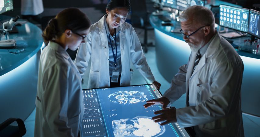 Modern Hospital Medical Cancer Research Center: Diverse Scientists Gathered Around Interactive Touch Screen Table With CT Scans Of Brain On Display.