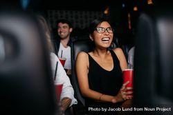 Young woman sitting in multiplex movie theater watching movie and laughing 4ZK6Ab