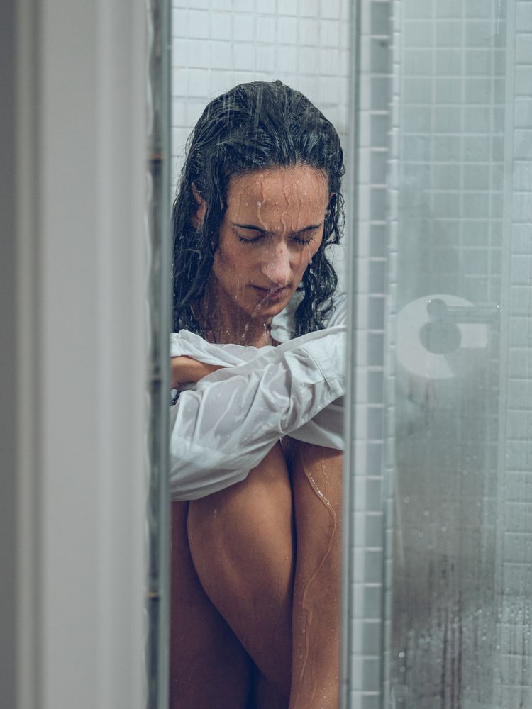 Tired woman sitting in shower cabin under pouring waterdrops