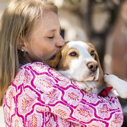 Blond adult woman kissing her Beagle dog while he is looking away.