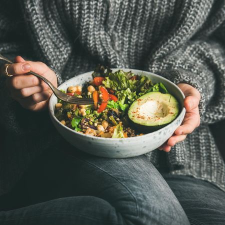 Woman in jeans and sweater eating fresh salad, square crop