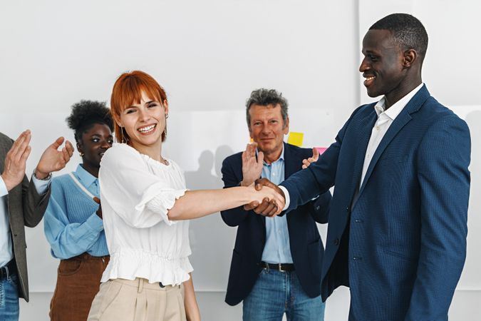 A moment of success as a red-haired white woman shakes hands with a Black colleague in suit