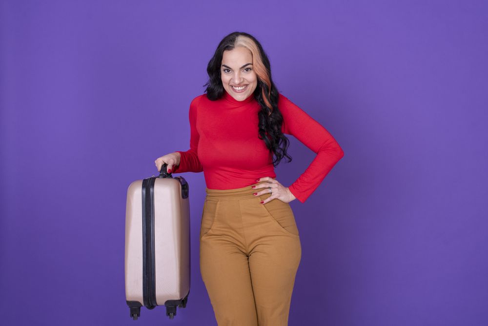 woman traveler holding her suitcase against purple background.