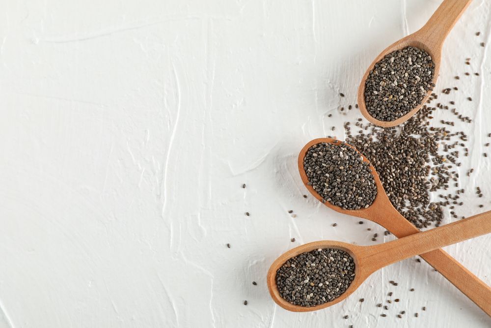 Wooden spoons and chia on neutral background, top view