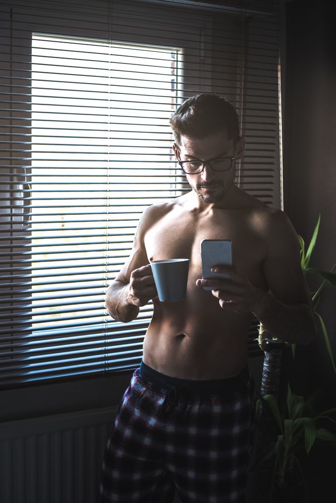 Man standing by a windows blind on the mobile phone