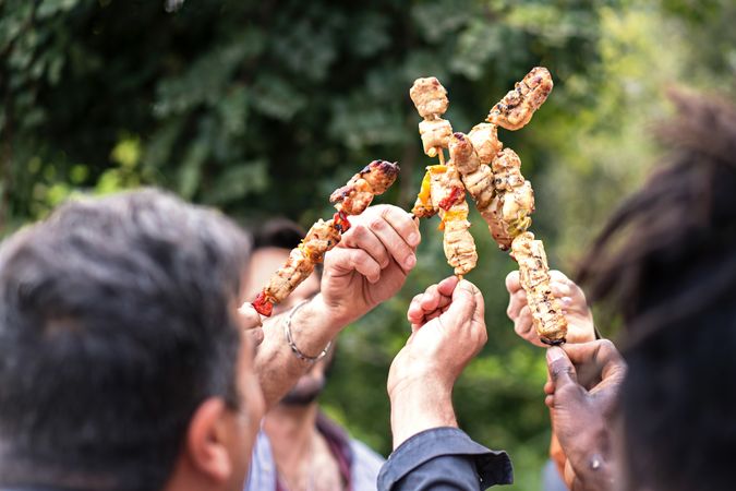 Close-up of hands toasting with delicious grilled skewers