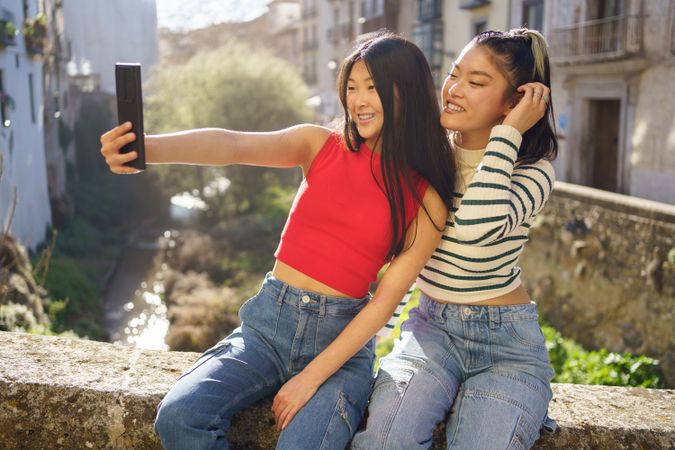 Two Asian women taking selfie on cellphone while sitting outside in Granada
