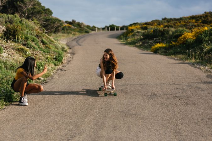 Latina woman taking photo of friend balancing on longboard