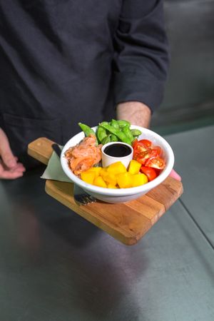 Unrecognizable chef showing fresh colorful poke bowl with salmon on restaurant kitchen
