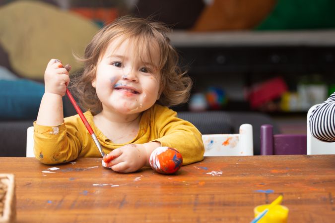 Toddler girl painting egg at table