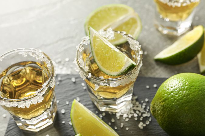 Tequila shots with salt and lime slices on grey background