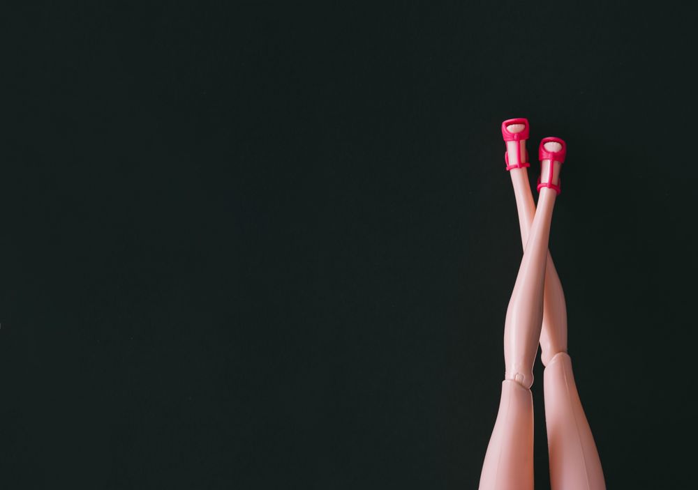 Doll legs in pink heels on dark background