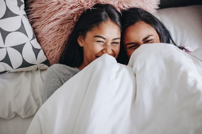 Two young women laughing while lying on bed during a sleepover