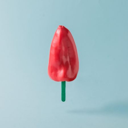 Red pepper with ice cream stick on pastel blue background