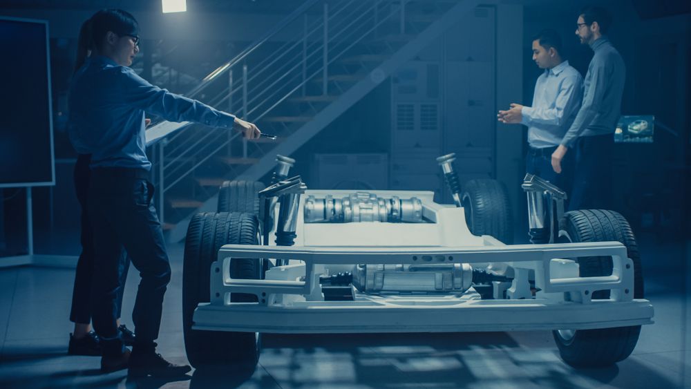 Automobile Engineers Working on Electric Car Chassis Platform, Using Tablet Computer Augmented Reality with CAD Software for 3D Concept.