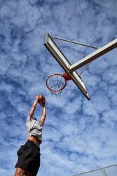 Man athlete jumping while dunking basketball against sky