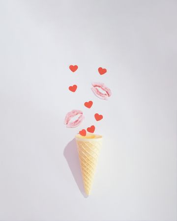 Kisses with small red hearts coming out of ice cream cone on a plain background
