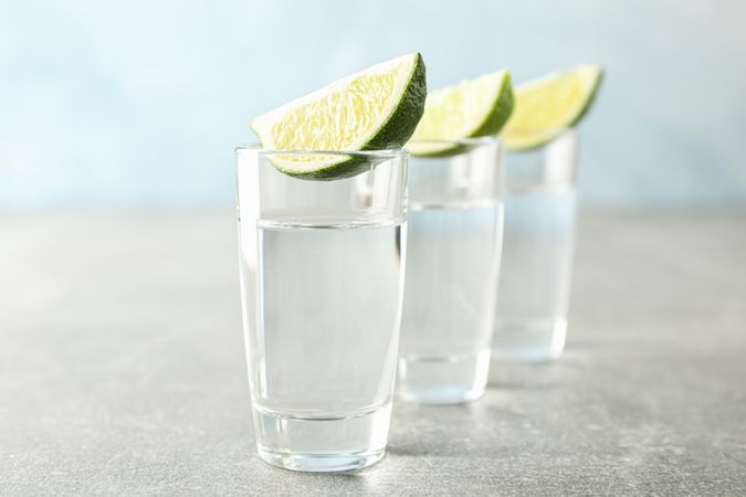 Tequila shots with lime slices on grey background