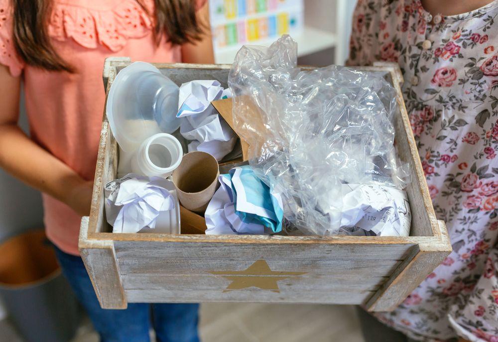 Two girls in ecology classroom showing box of waste to recycle