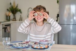 Glad kid putting sushi rolls on eyes at table