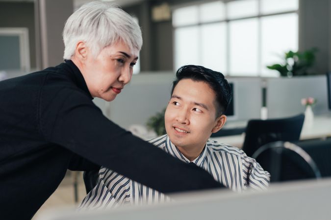 Mature Asian woman checking and discussing project on computer with male colleague