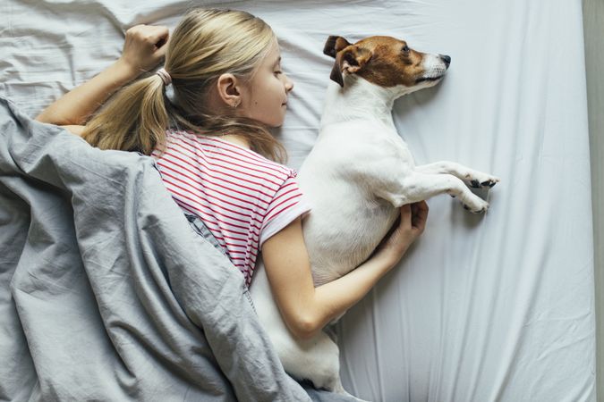Young girl cuddling with her dog in bed, top view