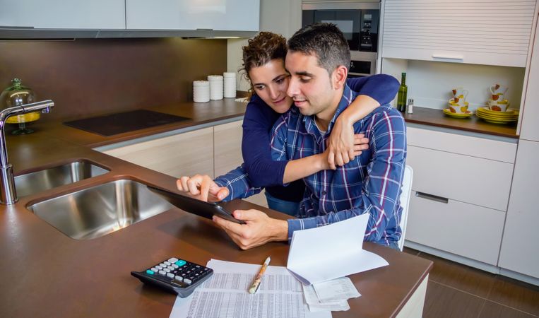 Woman holding man as they organize bills together in their kitchen