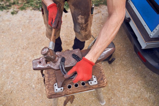 Blacksmith working on the anvil changing the horseshoe to a paw with tools