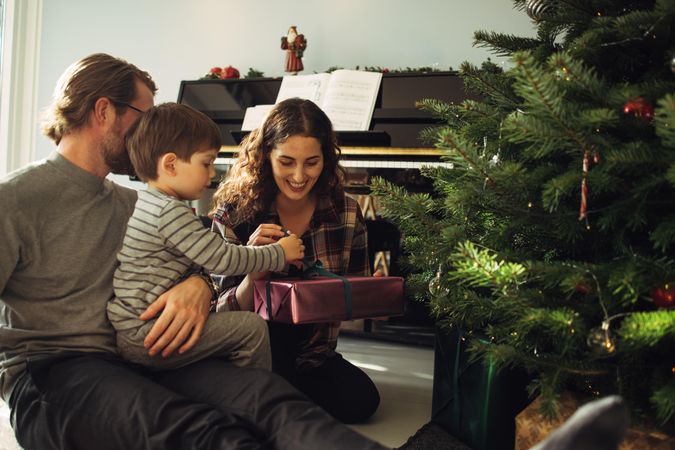 Boy opening his Christmas gift sitting with parents