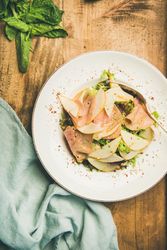 Top view of ham and pear in bowl, on wooden background with linen napkin