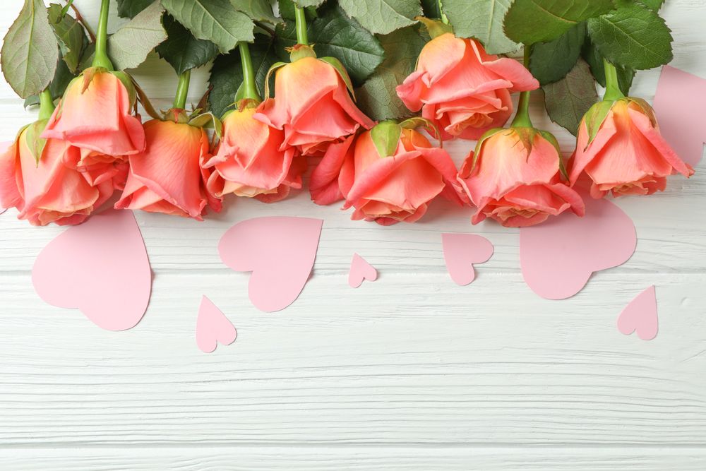 Beautiful orange roses with pink hearts on light background, space for text