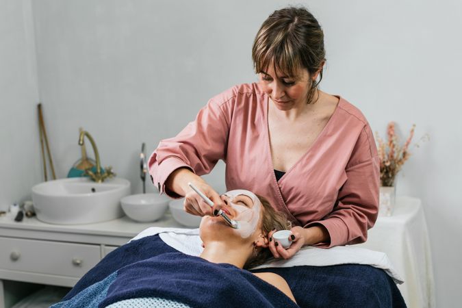 Professional beautician applying facial mask on face of client