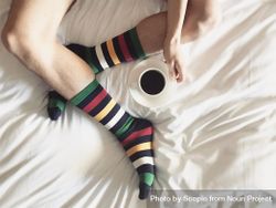 Person in a colorful socks holding a cup of coffee and sitting on a bed 5nmnZ0