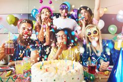 Friends celebrating at a birthday party with confetti, drinks and cake