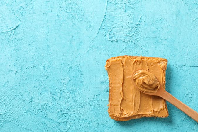 Peanut butter sandwich and spoon on color background, space for text and top view