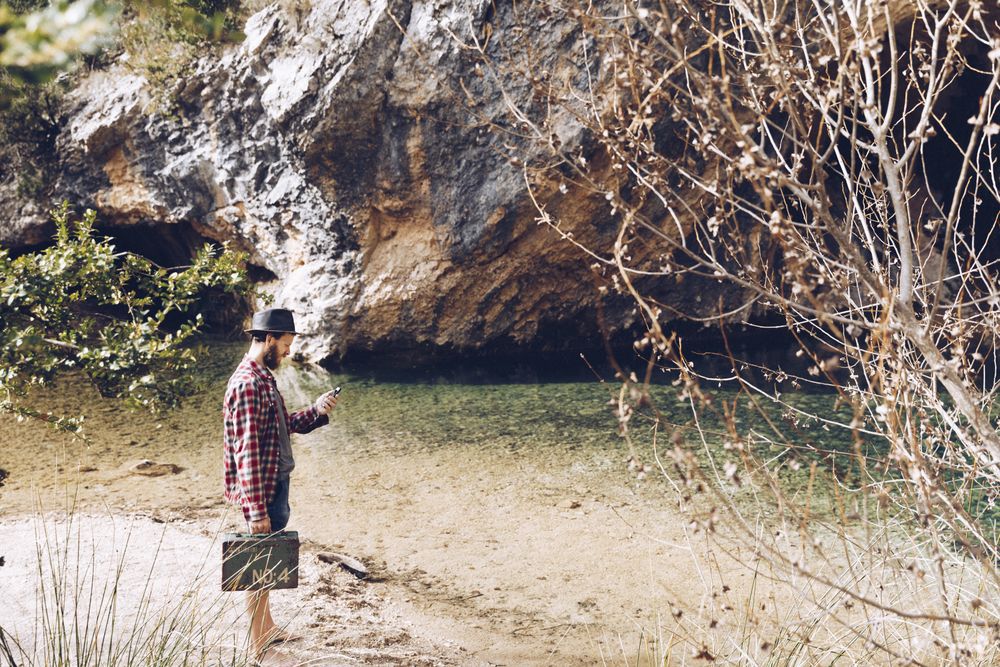 Man with case and smartphone on lake shore