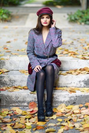 Female in warm winter clothes sitting among scattered fall leaves on park steps looking up at camera