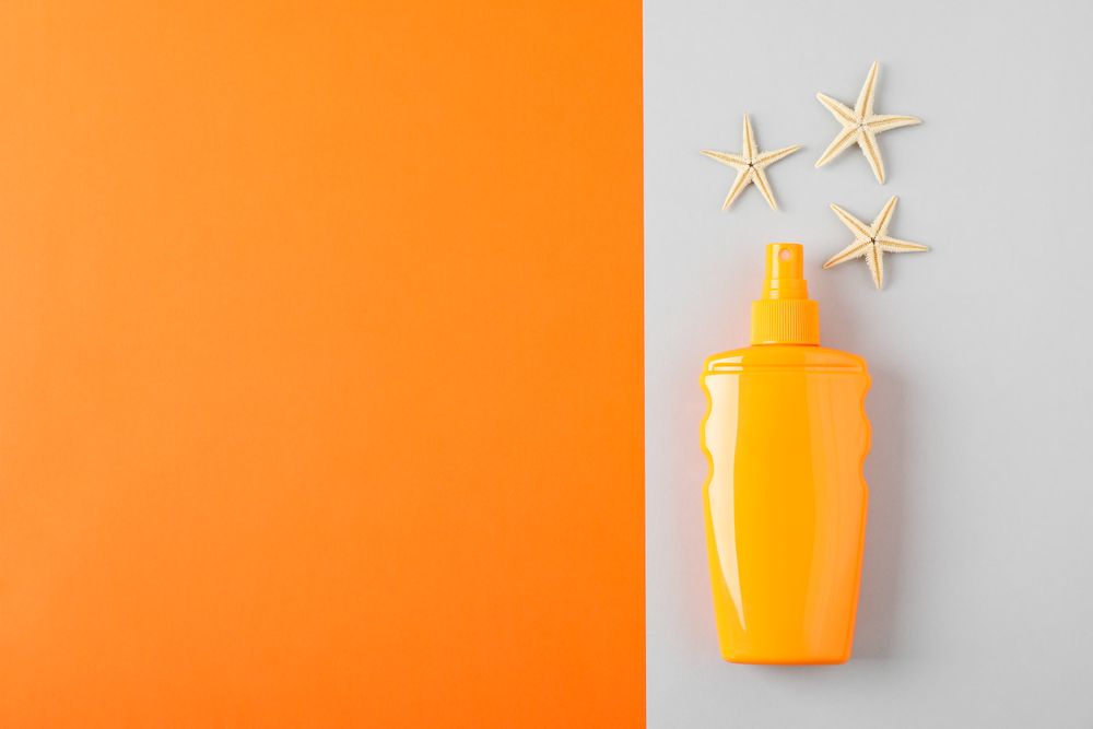 Composition with sunscreen spray and starfishes on two tone background, space for text. Summer vacation backdrop