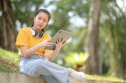 Woman wearing headphones on neck holding tablet looking at camera serious expression.